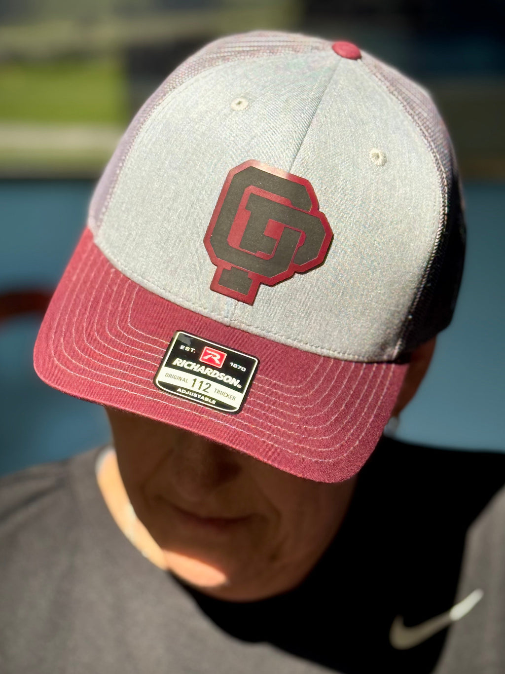 Person wearing a gray and red cap with a logo, outdoors.