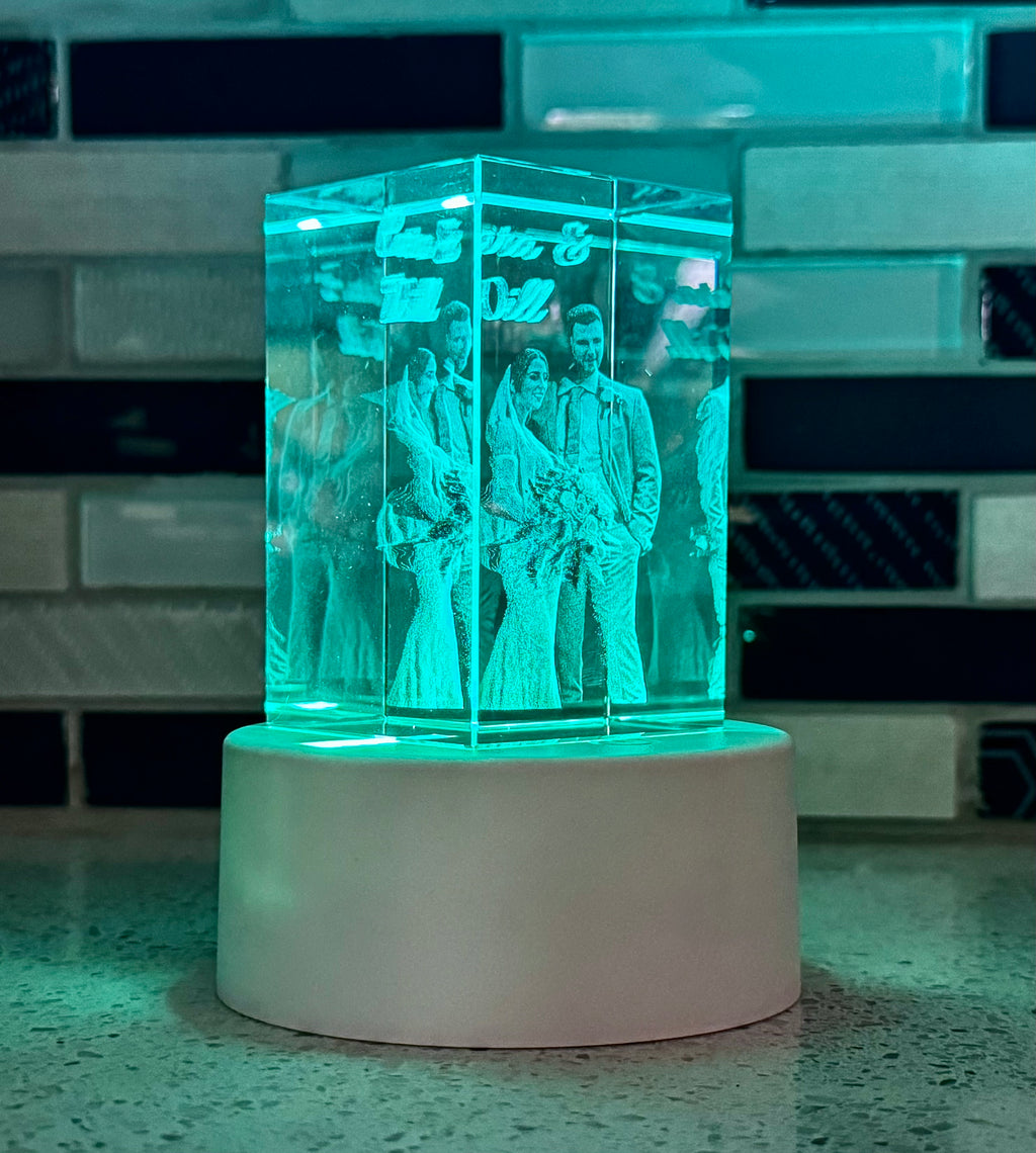 Transparent block with engraved figures on a white base against a tiled wall.