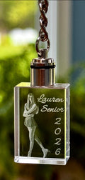 Crystal keychain with engraved photo and text 'Lauren Senior 2026' against a blurred green background.
