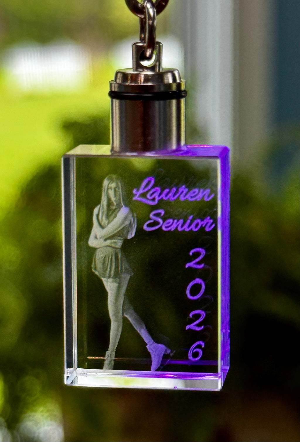 Crystal keychain with engraved image and text 'Lauren Senior 2026' on a blurred green background