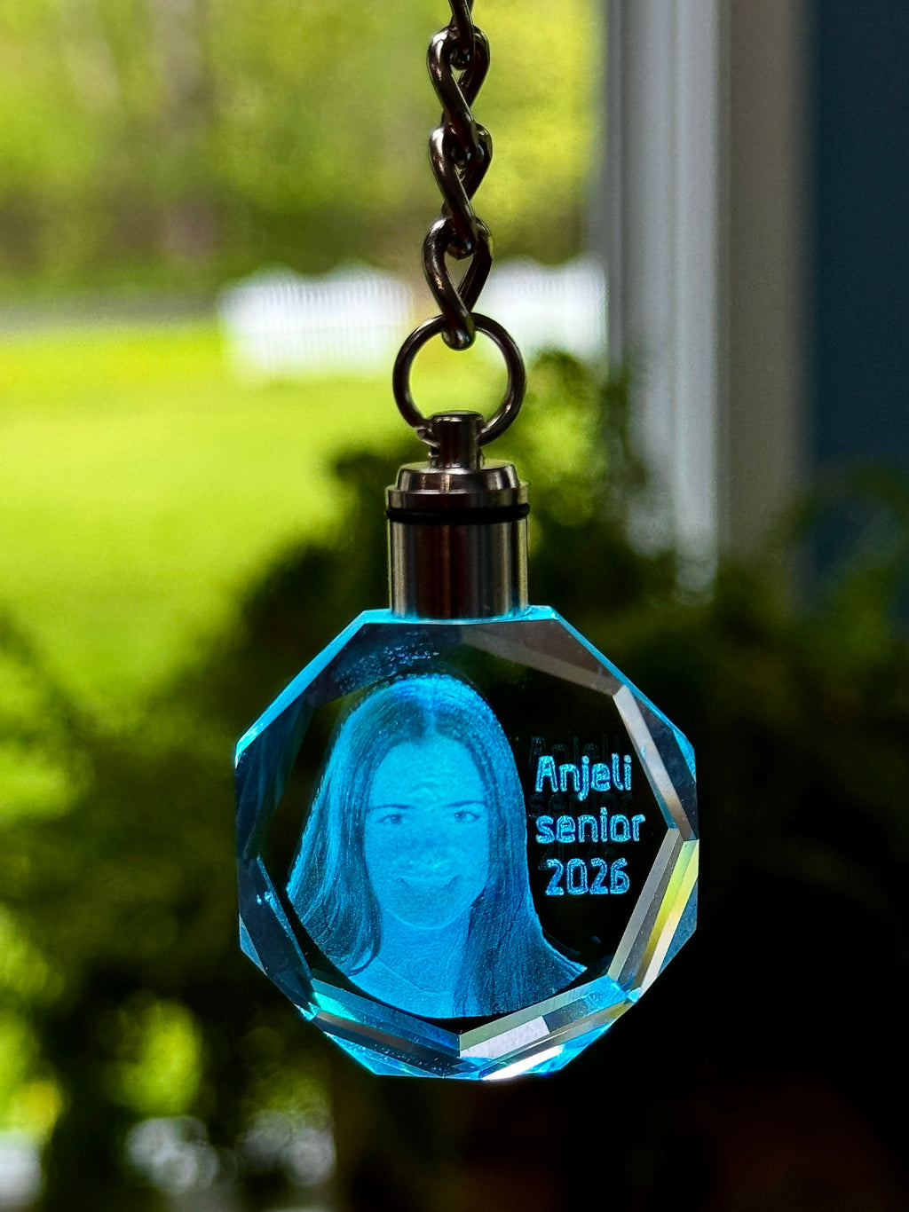 Blue crystal keychain with engraved text and portrait, outdoors.